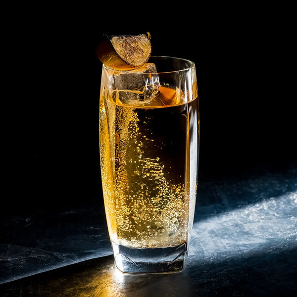 A whiskey cocktail in the Vawe Highball Glass with a collins ice cube and charred lemon wedge